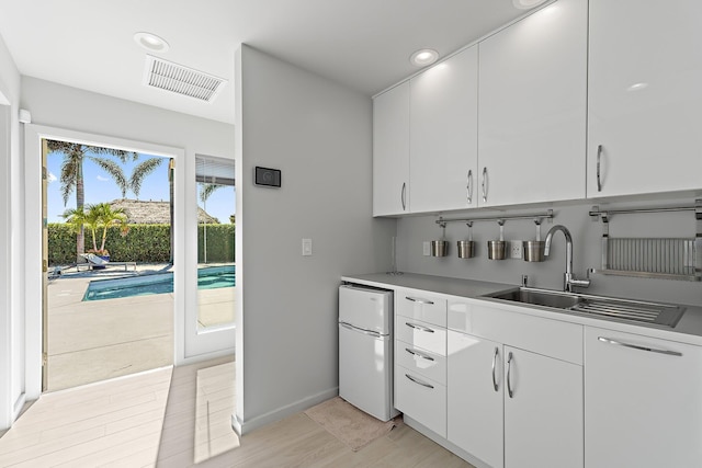 kitchen with visible vents, white cabinetry, freestanding refrigerator, and a sink