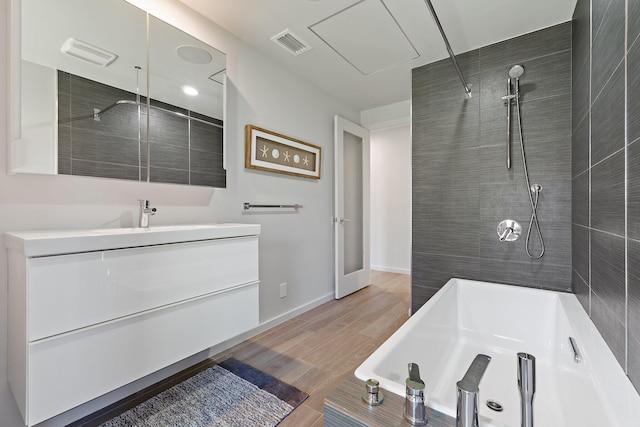 full bath featuring vanity, wood finished floors, a bathing tub, visible vents, and tiled shower