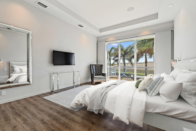 bedroom with a tray ceiling, wood finished floors, visible vents, and baseboards