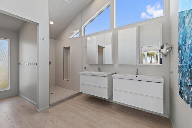 full bathroom featuring two vanities, a walk in shower, a sink, wood finished floors, and baseboards