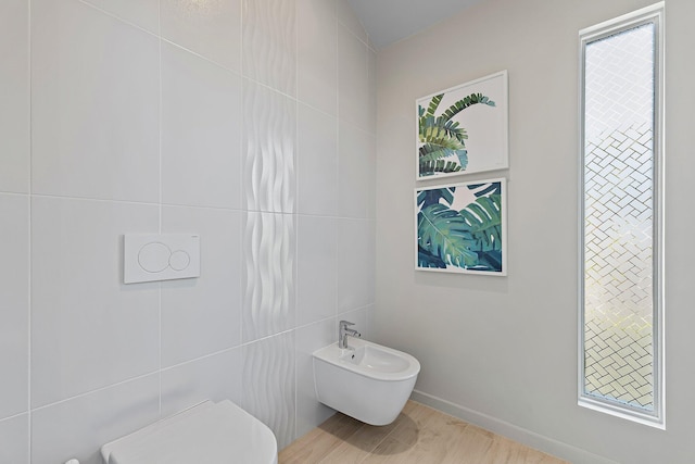 bathroom with wood finished floors, toilet, a bidet, and tile walls