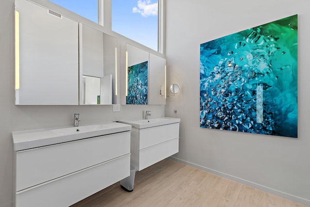 full bathroom featuring visible vents, baseboards, two vanities, wood finished floors, and a sink