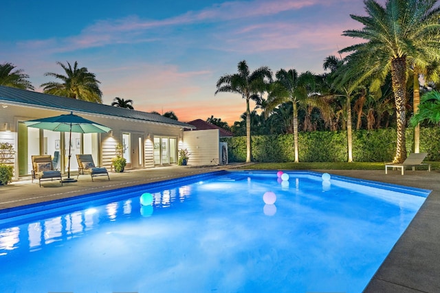 pool at dusk with an outdoor pool and a patio area