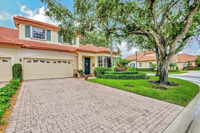 mediterranean / spanish home with a front yard, stucco siding, a garage, a tiled roof, and decorative driveway