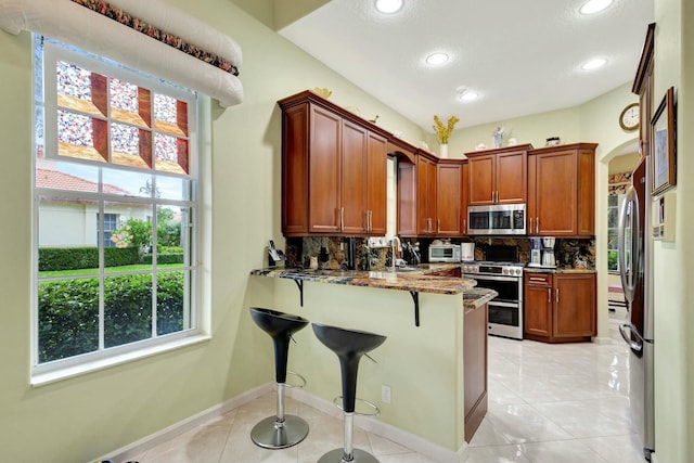 kitchen with tasteful backsplash, dark stone counters, a peninsula, arched walkways, and stainless steel appliances