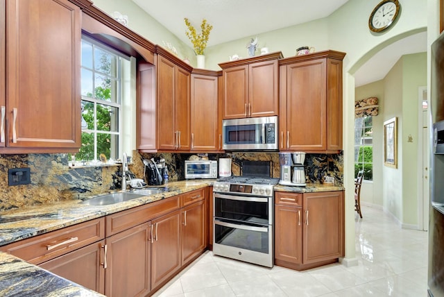 kitchen with a sink, decorative backsplash, light stone counters, and appliances with stainless steel finishes