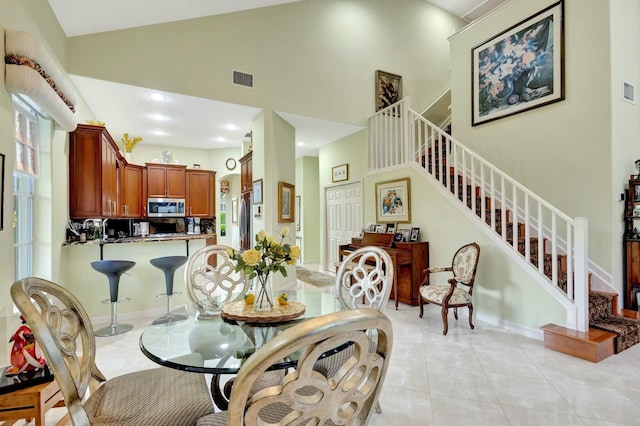 dining area featuring light tile patterned floors, baseboards, visible vents, high vaulted ceiling, and stairs