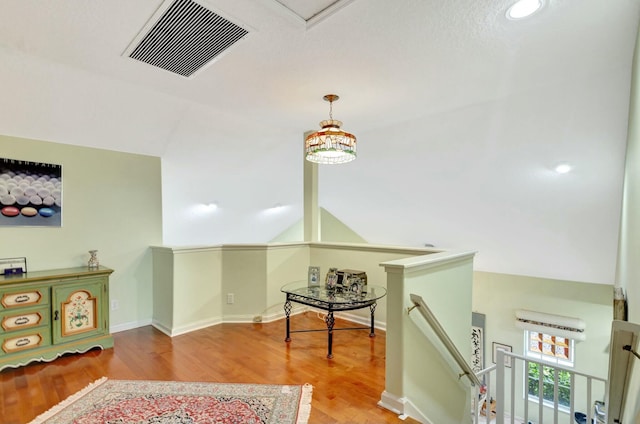 hallway with visible vents, baseboards, vaulted ceiling, an upstairs landing, and wood finished floors