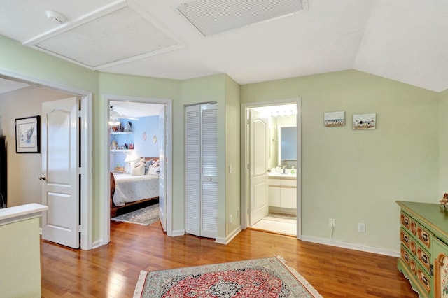 hallway featuring lofted ceiling, wood finished floors, visible vents, and baseboards