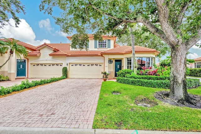 mediterranean / spanish-style house with stucco siding, a tile roof, decorative driveway, and a garage