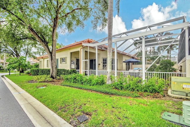 view of side of home with a lanai, a tiled roof, a yard, and stucco siding