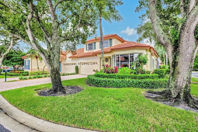 mediterranean / spanish house featuring stucco siding, driveway, a tile roof, and a front yard