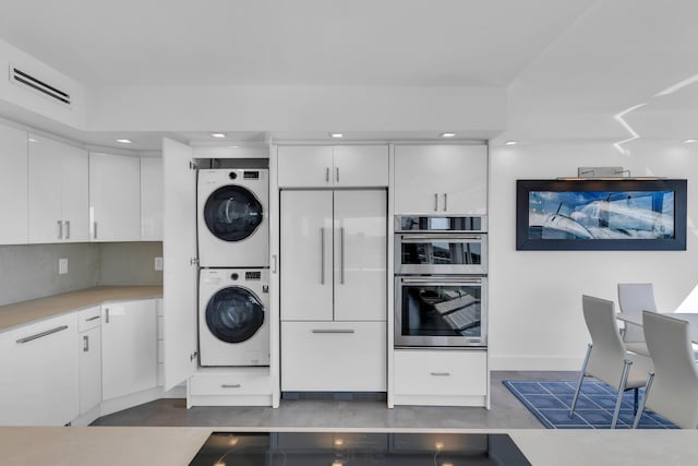 kitchen with stacked washer / dryer, visible vents, built in refrigerator, stainless steel double oven, and white cabinetry