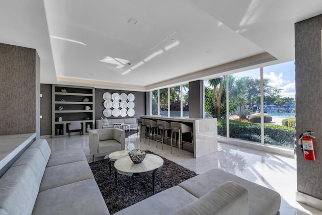 living area with floor to ceiling windows, marble finish floor, and a tray ceiling