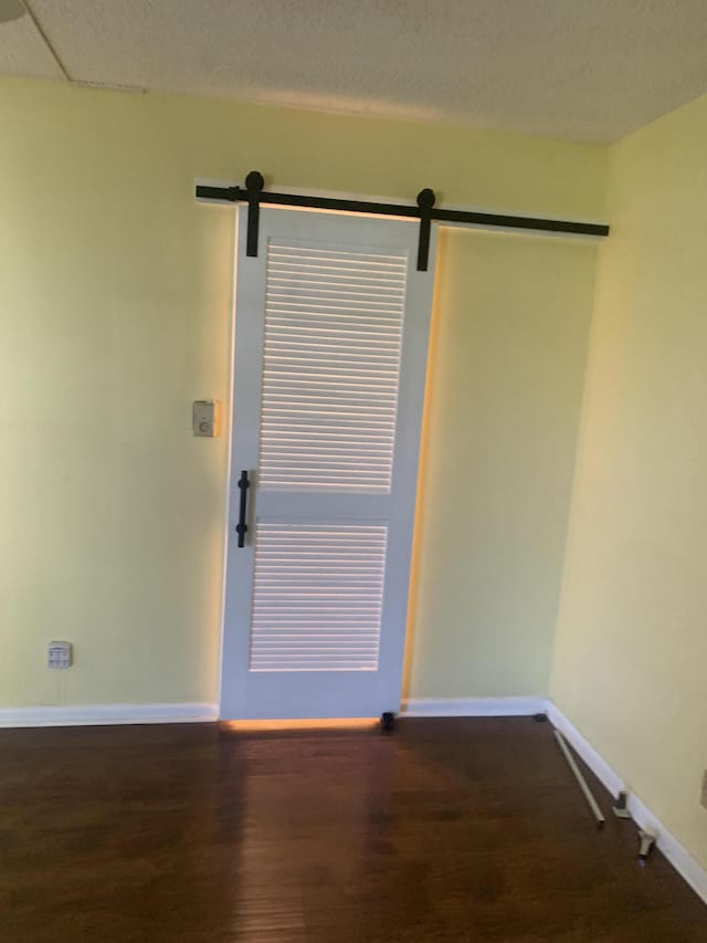 empty room featuring a barn door, baseboards, a textured ceiling, and wood finished floors