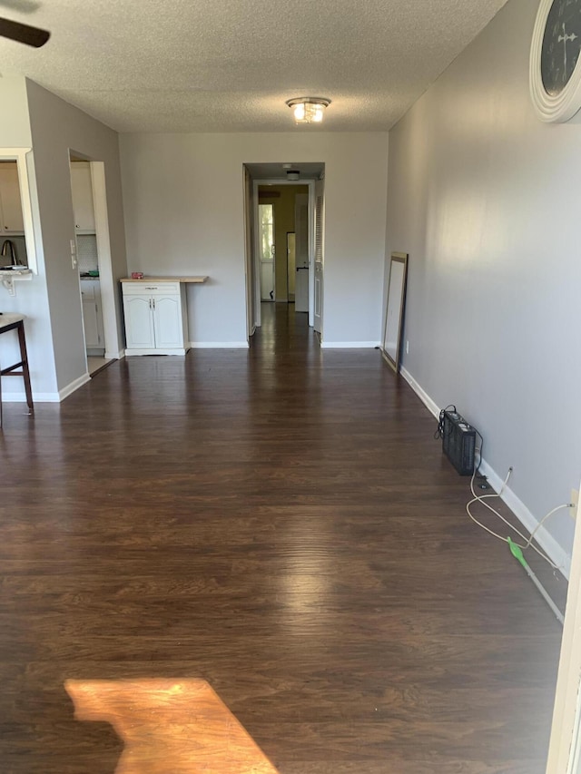 unfurnished living room featuring baseboards, dark wood-type flooring, a ceiling fan, and a textured ceiling