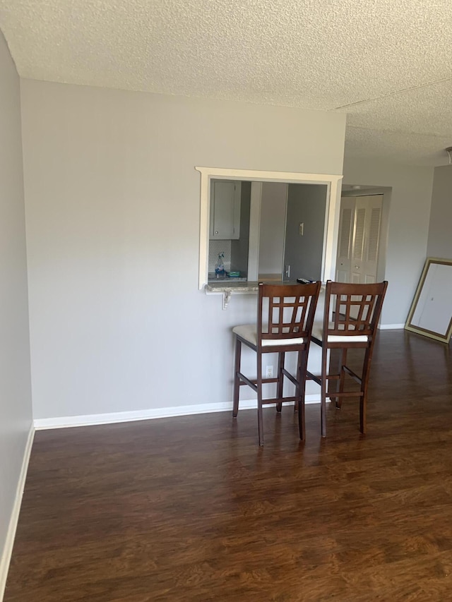 dining area with baseboards, a textured ceiling, and dark wood finished floors