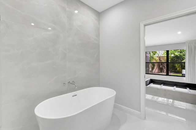 full bath featuring tile walls, a freestanding tub, and baseboards