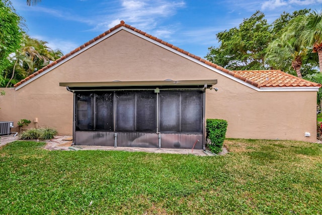 back of property featuring central AC unit, a lawn, a tiled roof, and stucco siding