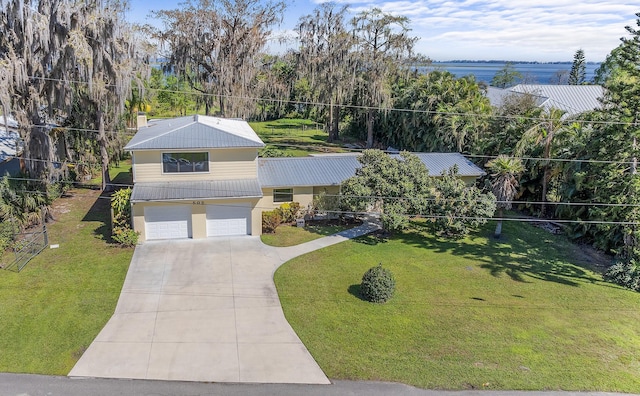 view of front facade with an attached garage, concrete driveway, metal roof, and a front yard