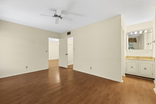 unfurnished bedroom featuring visible vents, baseboards, ensuite bathroom, wood finished floors, and a textured ceiling