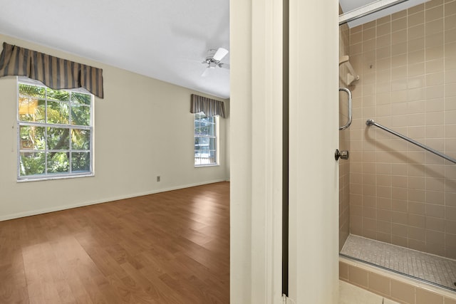 bathroom featuring a ceiling fan, wood finished floors, baseboards, and tiled shower