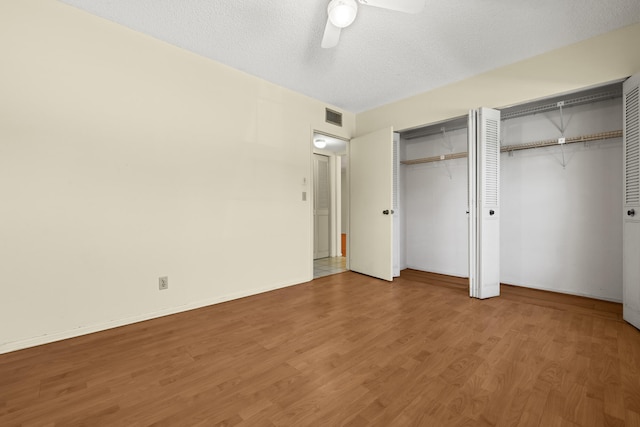 unfurnished bedroom with wood finished floors, baseboards, visible vents, a textured ceiling, and two closets