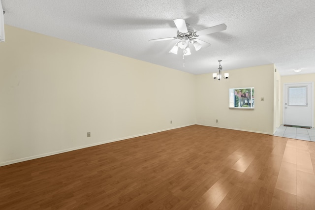 unfurnished room featuring light wood finished floors, ceiling fan with notable chandelier, a textured ceiling, and baseboards