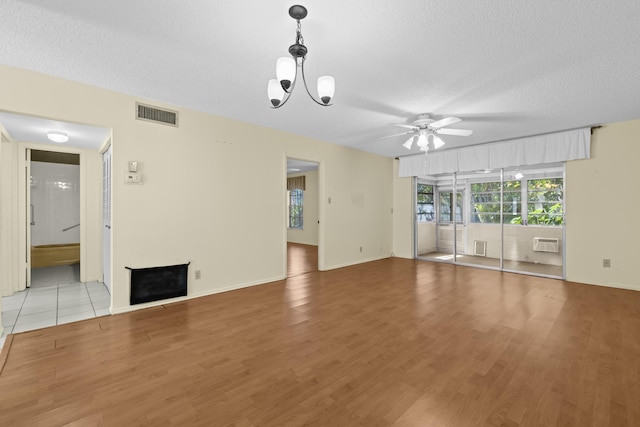 unfurnished living room with visible vents, a wall mounted AC, a fireplace, light wood-style floors, and a textured ceiling