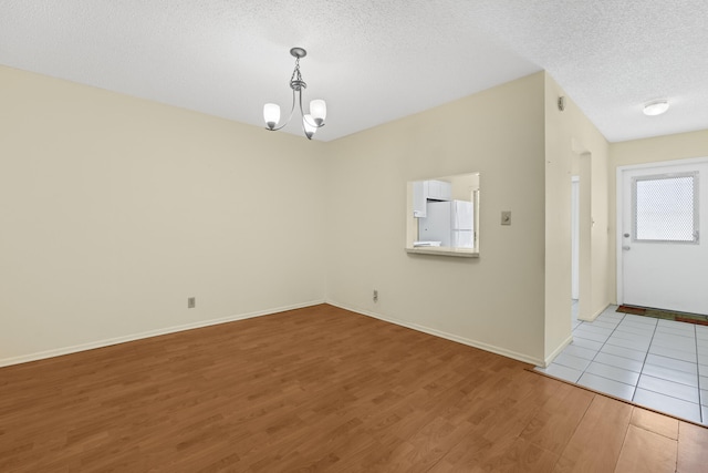 unfurnished room with a chandelier, a textured ceiling, baseboards, and wood finished floors