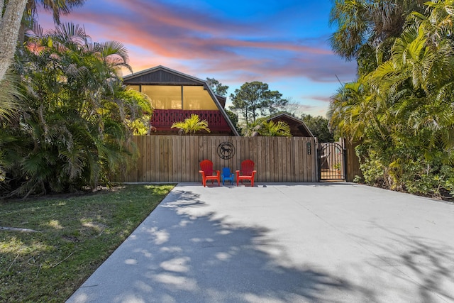 patio terrace at dusk featuring a carport, a gate, fence, and driveway