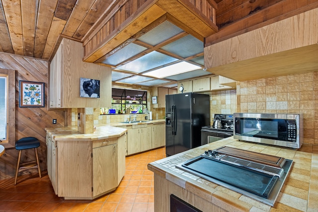 kitchen featuring black appliances, a sink, light tile patterned floors, decorative backsplash, and tile counters