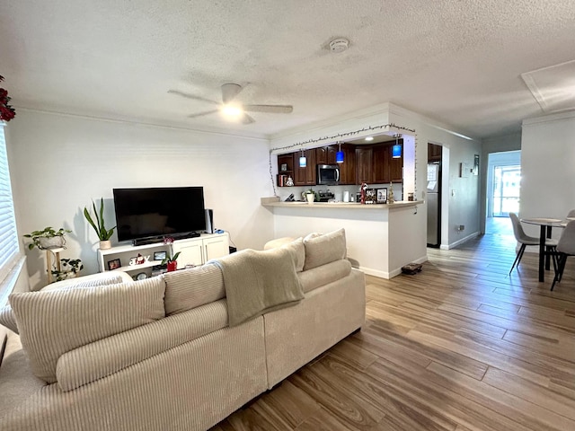 living room with a ceiling fan, wood finished floors, baseboards, and a textured ceiling