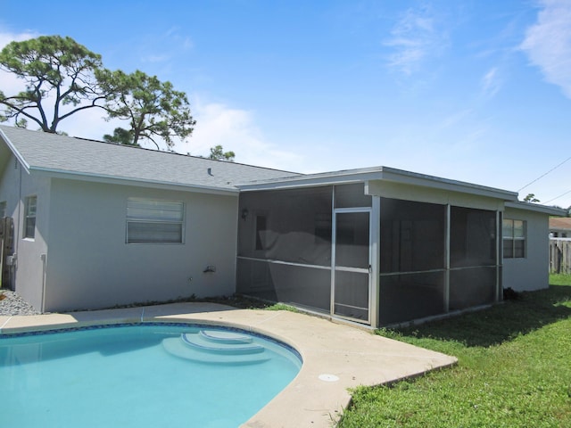 back of property with an outdoor pool, stucco siding, a lawn, and a sunroom