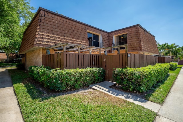 view of side of home featuring mansard roof, brick siding, and fence