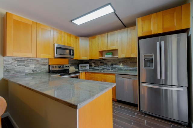 kitchen featuring light stone counters, decorative backsplash, a peninsula, stainless steel appliances, and a sink