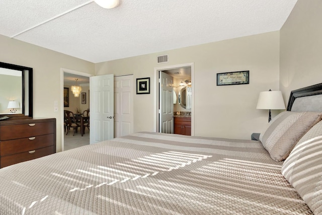 bedroom featuring connected bathroom, visible vents, and a textured ceiling