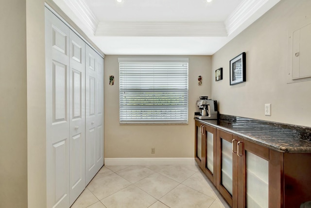 kitchen with dark countertops, light tile patterned floors, crown molding, and a raised ceiling