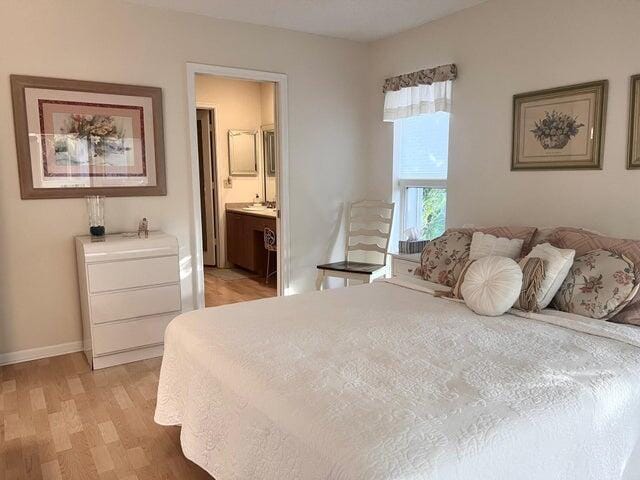 bedroom with connected bathroom, baseboards, and light wood-style flooring