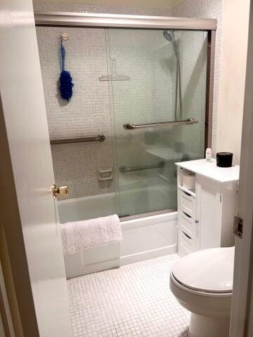 bathroom featuring tile patterned floors, toilet, and bath / shower combo with glass door