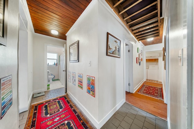 corridor featuring baseboards, washing machine and dryer, a wall mounted air conditioner, wooden ceiling, and tile patterned floors