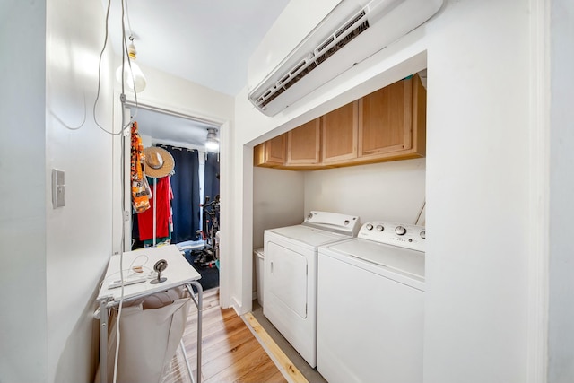 washroom featuring cabinet space, light wood-type flooring, a wall unit AC, and separate washer and dryer