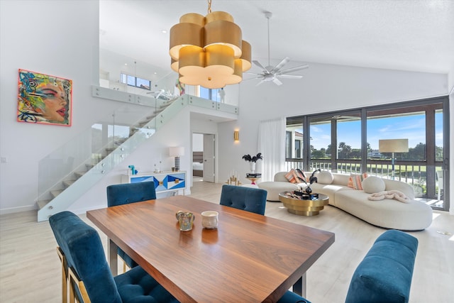 dining room with stairs, light wood-style flooring, baseboards, and high vaulted ceiling