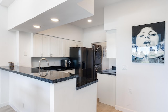 kitchen with a peninsula, recessed lighting, black fridge with ice dispenser, stacked washer / drying machine, and white cabinetry