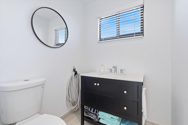 half bathroom with toilet, wood finished floors, and vanity