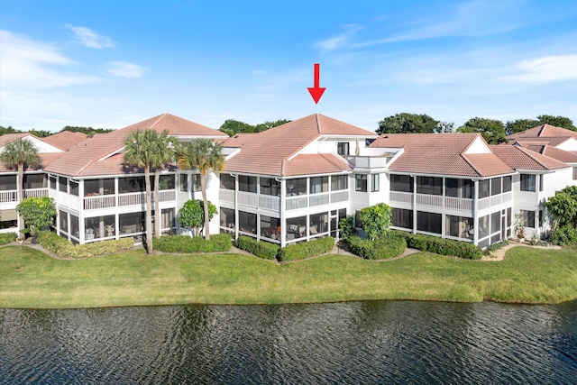 back of house featuring a water view, a lawn, a tile roof, and a sunroom