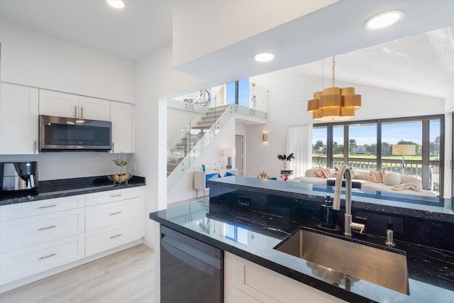 kitchen with lofted ceiling, a sink, white cabinetry, stainless steel microwave, and decorative light fixtures