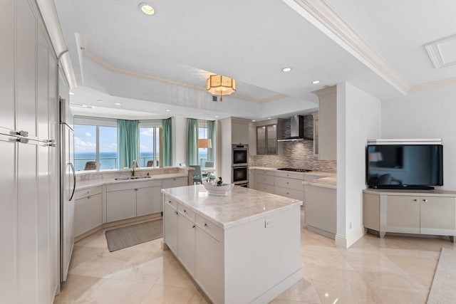 kitchen with a sink, ornamental molding, decorative backsplash, wall chimney exhaust hood, and a center island