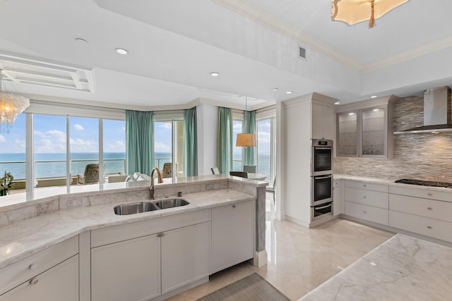 kitchen with visible vents, backsplash, wall chimney range hood, ornamental molding, and a sink