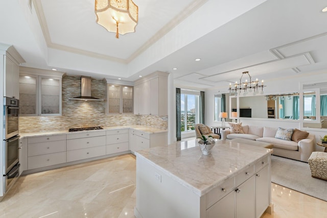 kitchen with a chandelier, open floor plan, wall chimney exhaust hood, and a raised ceiling